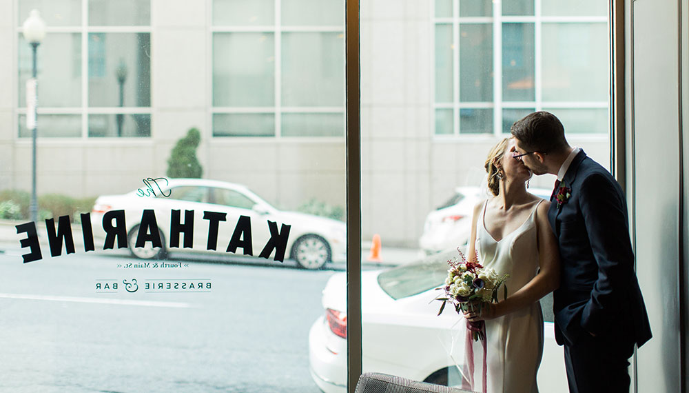 bride and groom kissing inside restaurant next to glass window with restaurant logo